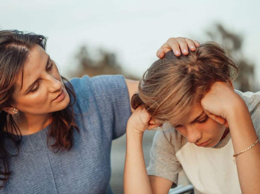 Une mère pose la main sur la tête de son fils adolescent, abattu, la tête entre les mains